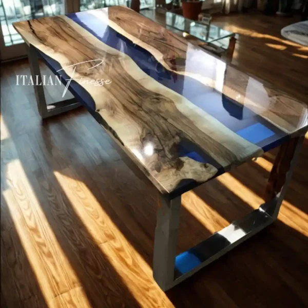 Tavolo in legno di ulivo con inserti in resina blu trasparente effetto fiume, struttura in metallo, illuminato dalla luce naturale in un salotto moderno.