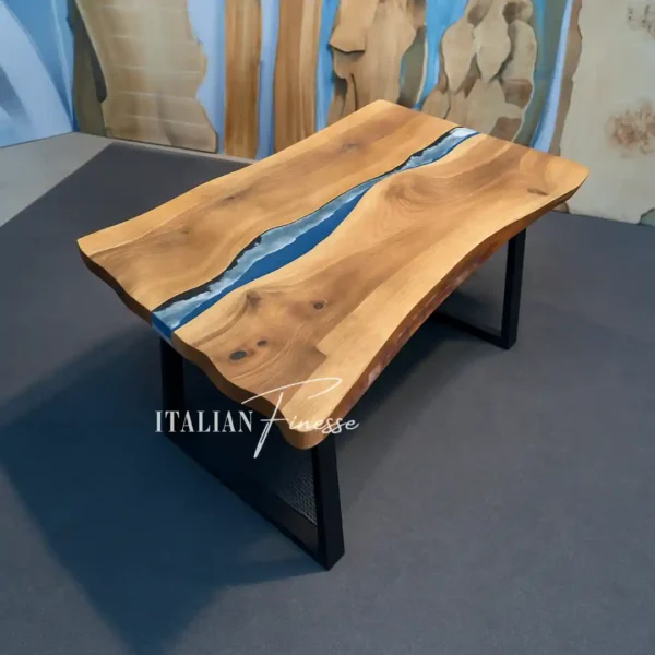 Tavolo rettangolare in noce europeo con bordo irregolare e inserto centrale in resina azzurra effetto fiume, ambientato su pavimento scuro e parete decorata.